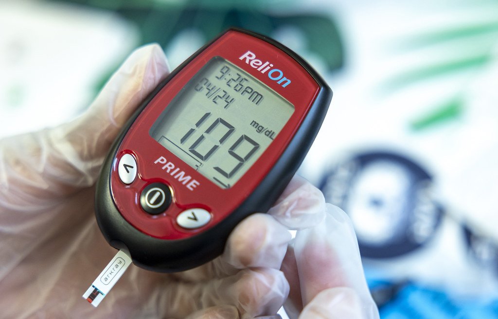 Hand holding a blood glucose meter showing a reading of 109