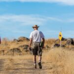 An older man and woman walking side by side on a dry dirt hiking trail under a blue sky