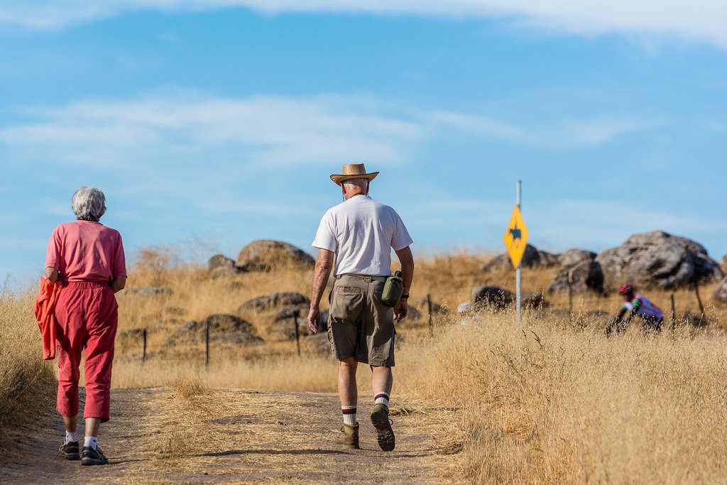 Older couple walking side by side on a dirt trail on a sunny day