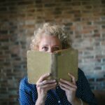 Portrait of a senior blond woman hiding behind an open old book