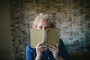 Portrait of a senior blond woman hiding behind an open old book