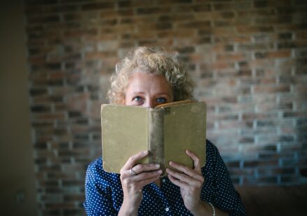 Portrait of a senior blond woman hiding behind an open old book