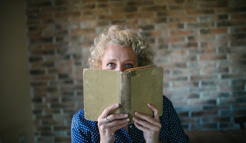 Portrait of a senior blond woman hiding behind an open old book