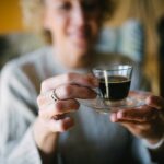 Smiling senior woman holding a glass of espresso coffee closeup