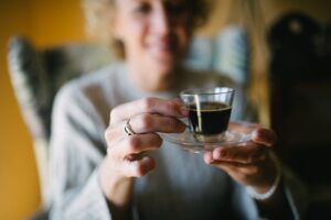 Smiling senior woman holding a glass of espresso coffee closeup