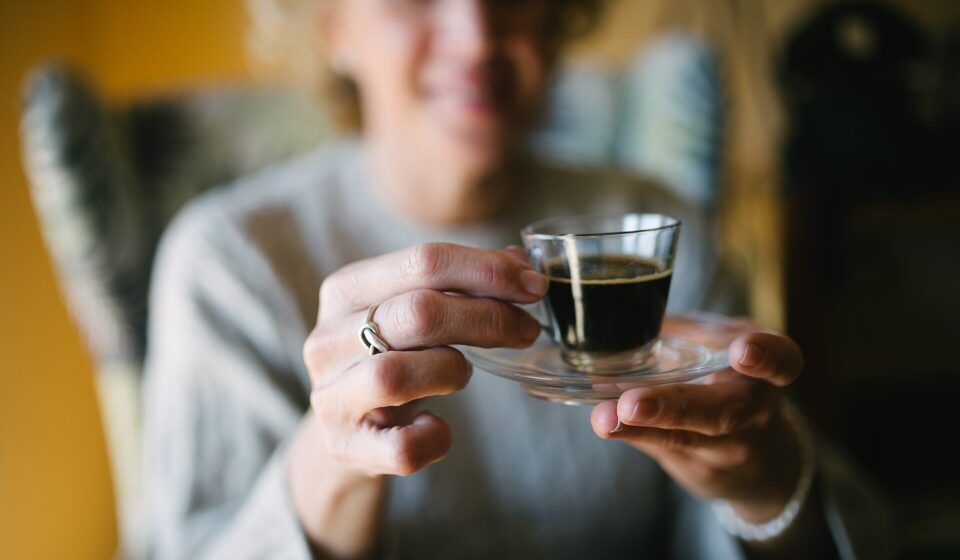 Smiling senior woman holding a glass of espresso coffee closeup