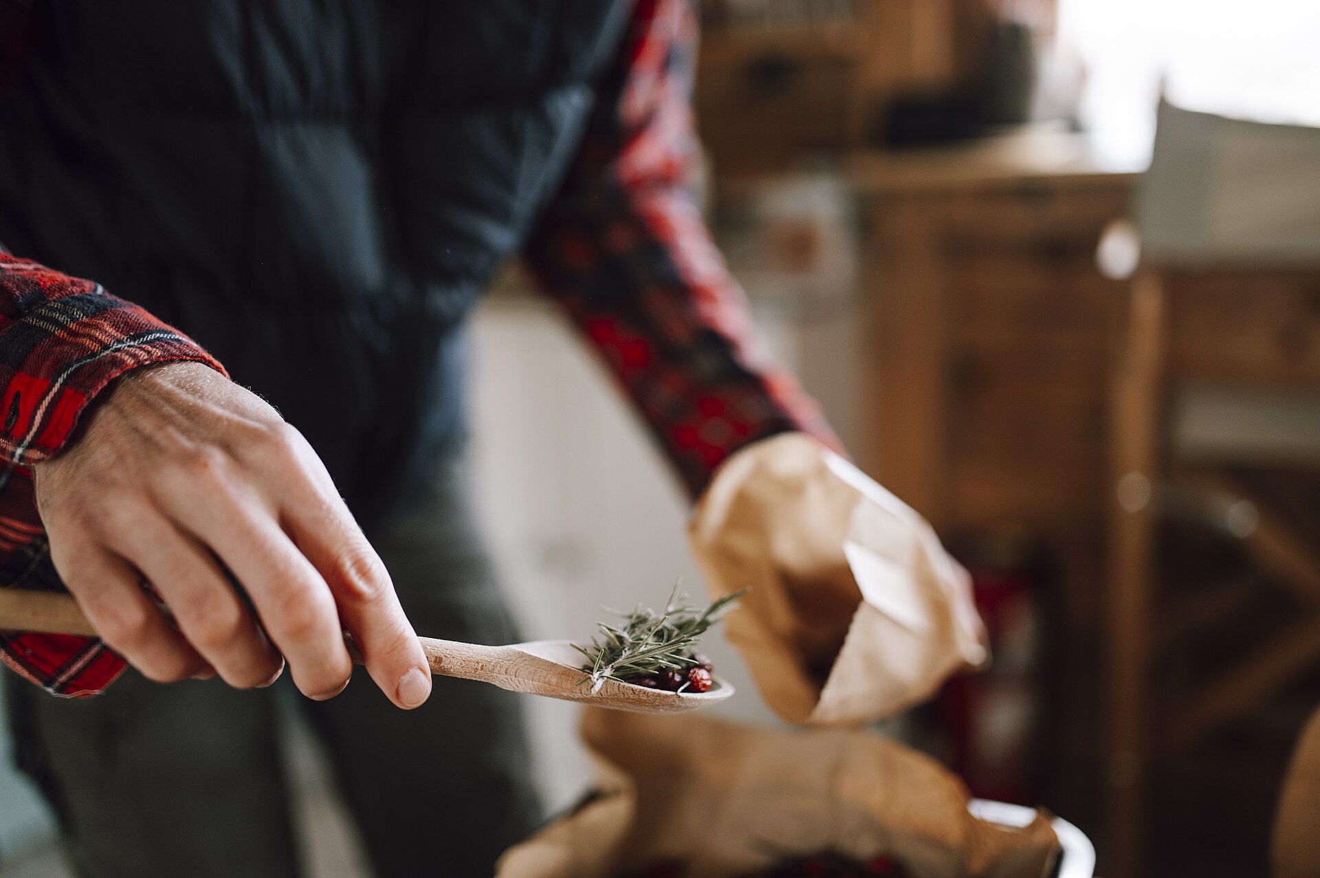 Hands adding fresh herbs from a wooden spoon to a pot of beans in a kitchen