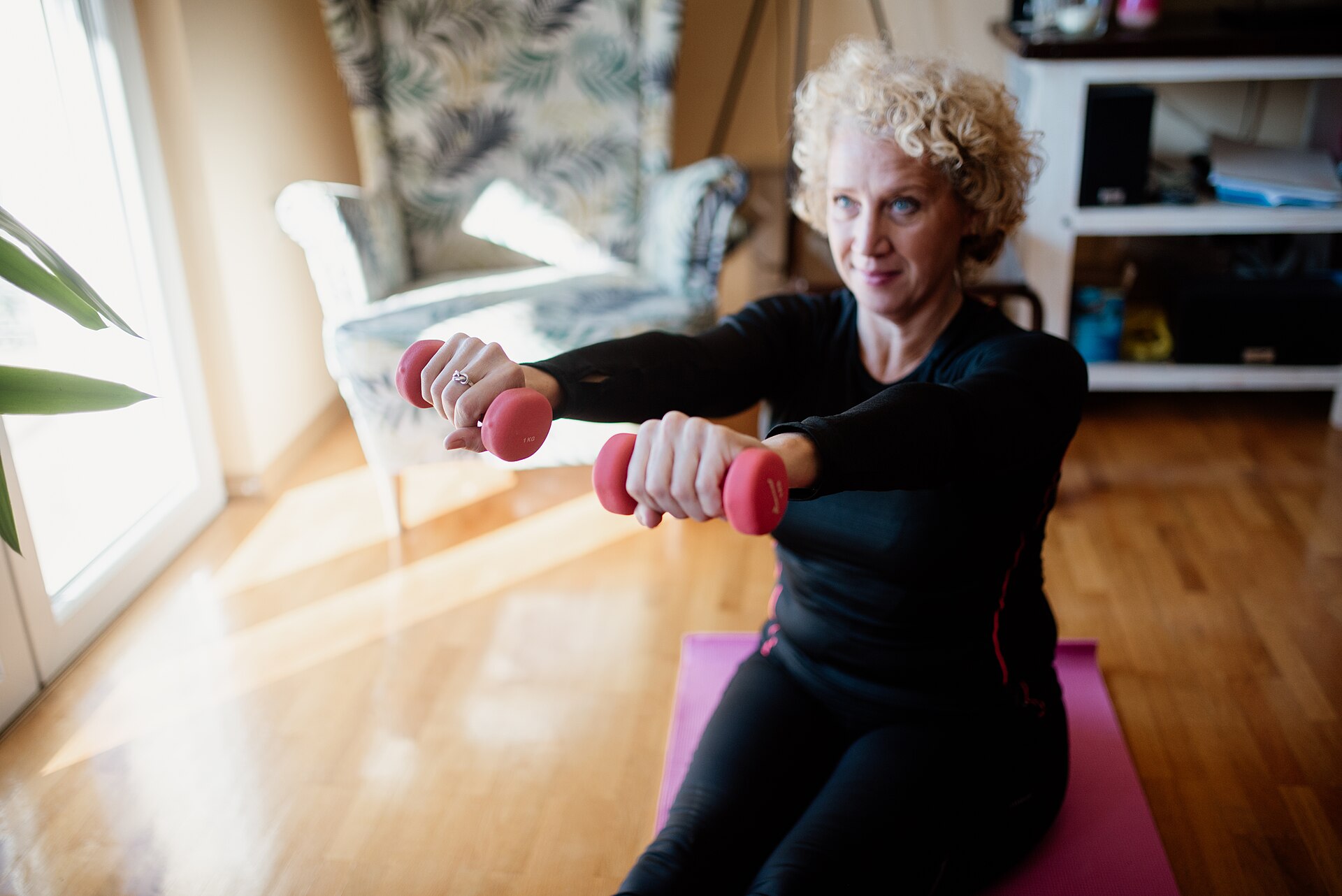 Senior woman exercising with light dumbbells on a mat at home