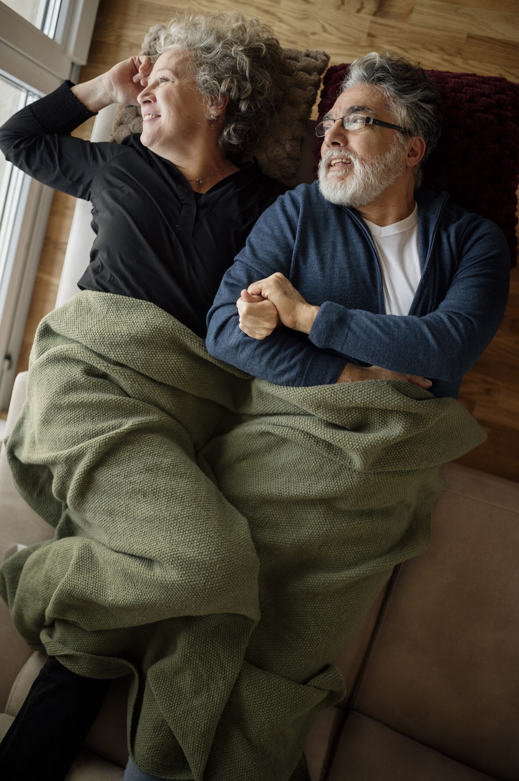 Older couple resting together on a couch under a blanket at home