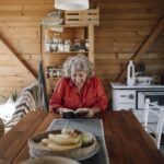 Senior woman reading a book at a wooden table in a cozy cabin