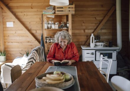 Senior woman reading a book at a wooden table in a cozy cabin