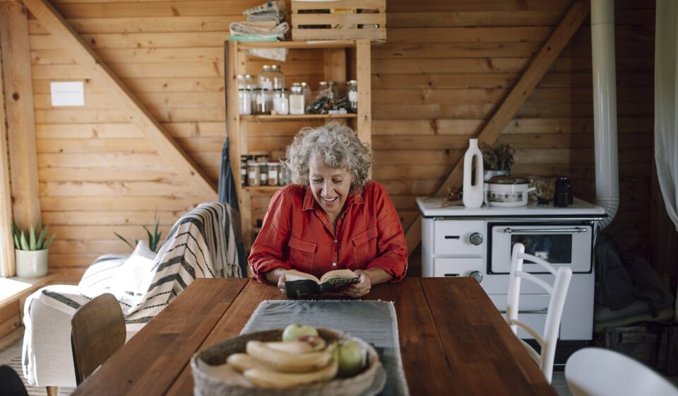 Senior woman reading a book at a wooden table in a cozy cabin