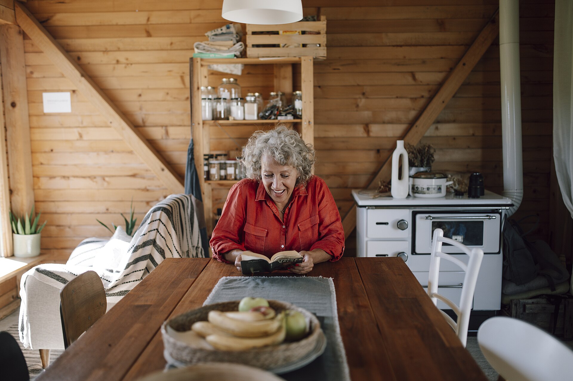 Senior woman reading a book at a wooden table in a cabin
