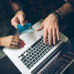 Older couple at a laptop, one holding a payment card while they review bills together