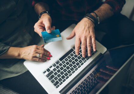 Older couple at a laptop, one holding a payment card while they review bills together