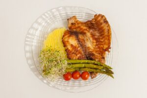 A plate of grilled chicken, asparagus, tomatoes and grains