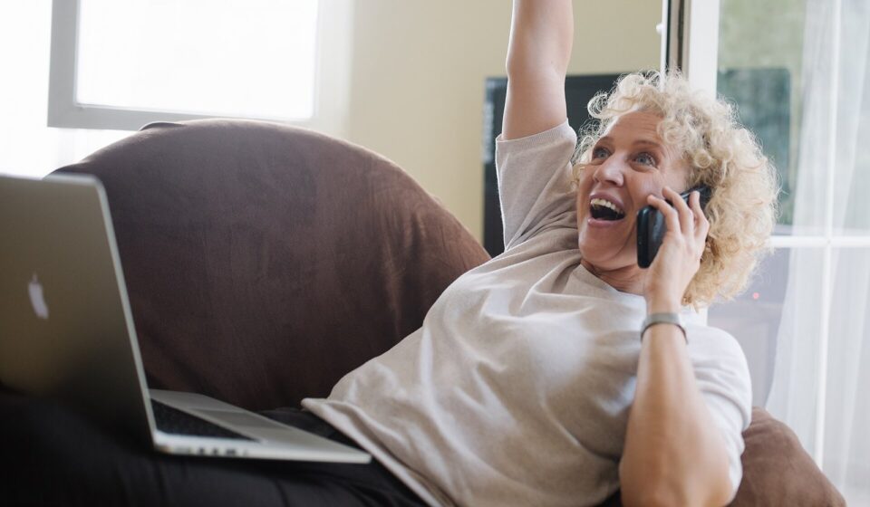 Medicare Flex Card for 2027: What It Really Is, Who Gets One, and the Ads to Ignore Senior woman with a laptop on her lap, talking on the phone and raising her arm in celebration