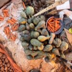 Green pumpkins, orange carrots and sweet potatoes laid out for sale at an outdoor market