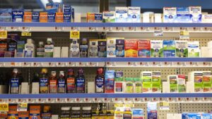 Shelves of over-the-counter pain relievers and cold medicines in a grocery store pharmacy aisle