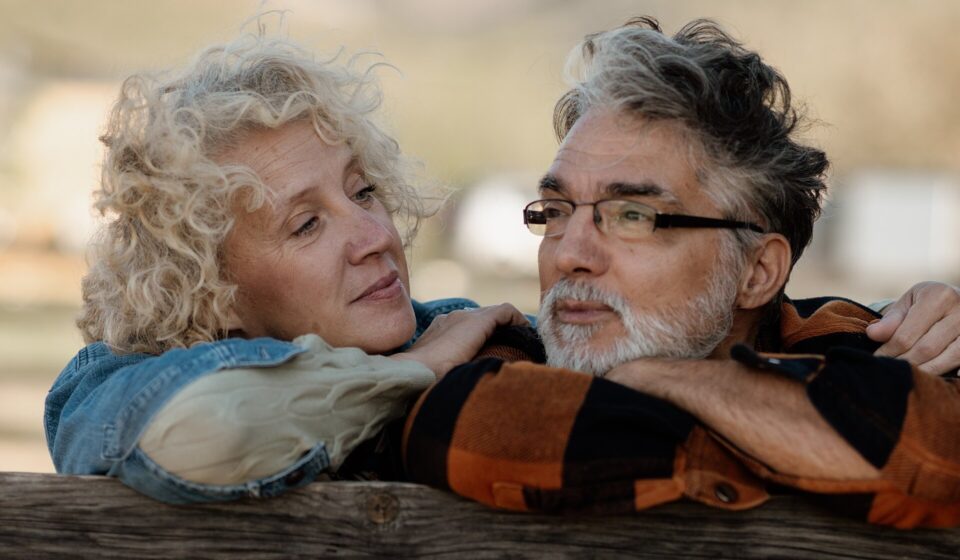 Senior couple standing close together by a wooden farm fence