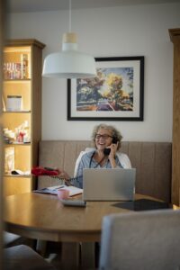 Older woman talking on the phone while sitting at a table with a laptop