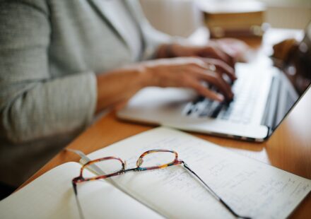 Reading glasses resting on handwritten notes beside a laptop