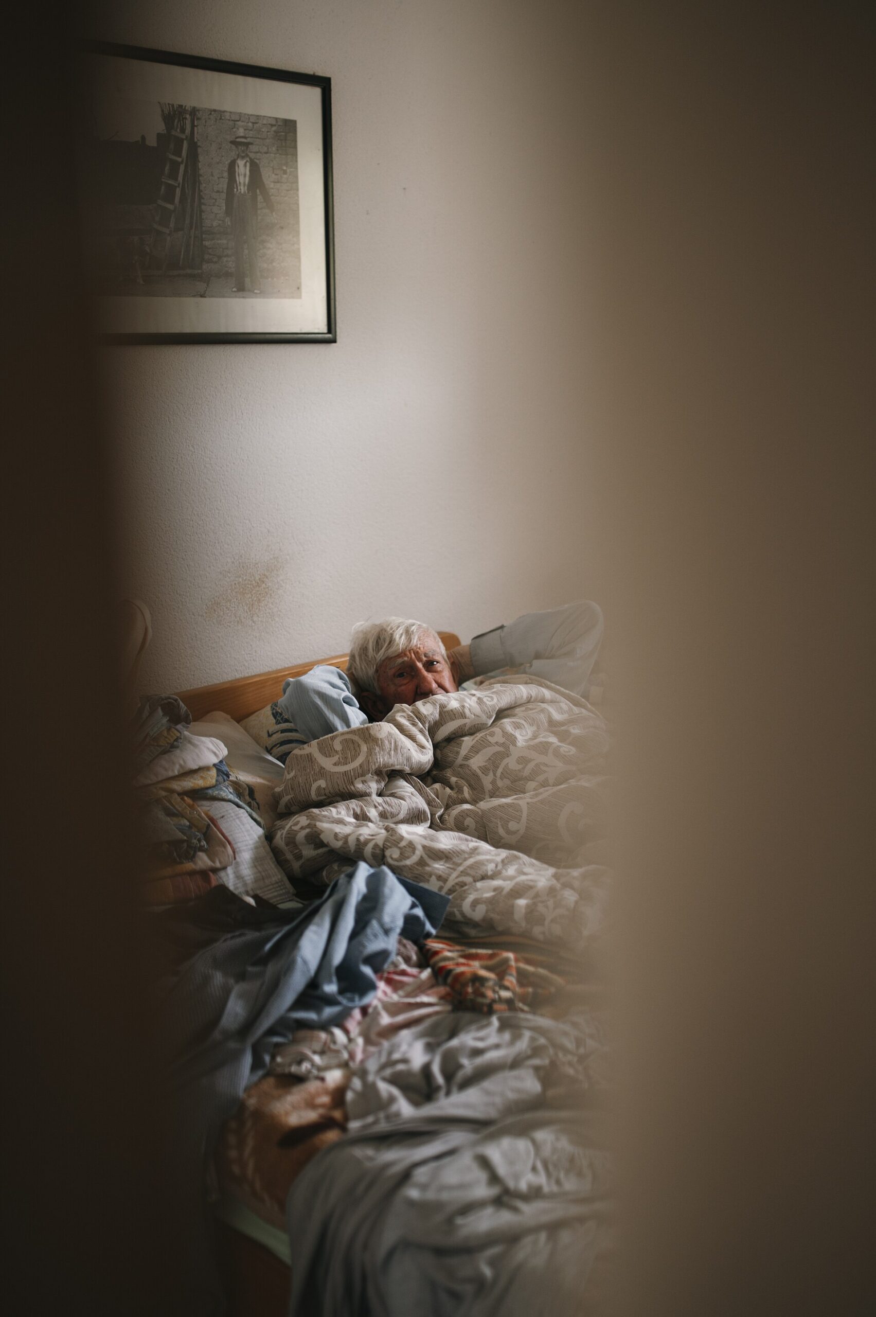 Older man resting in bed at home under blankets
