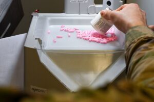 A pharmacist pours tablets into an automated pill counter while filling a prescription