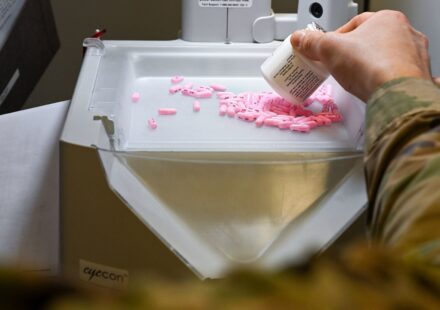A pharmacist pours tablets into an automated pill counter while filling a prescription