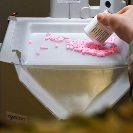 A pharmacist pours tablets into an automated pill counter while filling a prescription