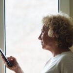 Older woman standing by a window checking her phone
