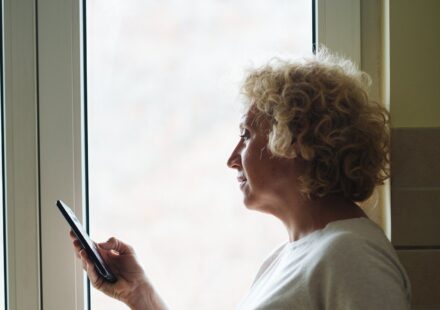 Older woman standing by a window checking her phone