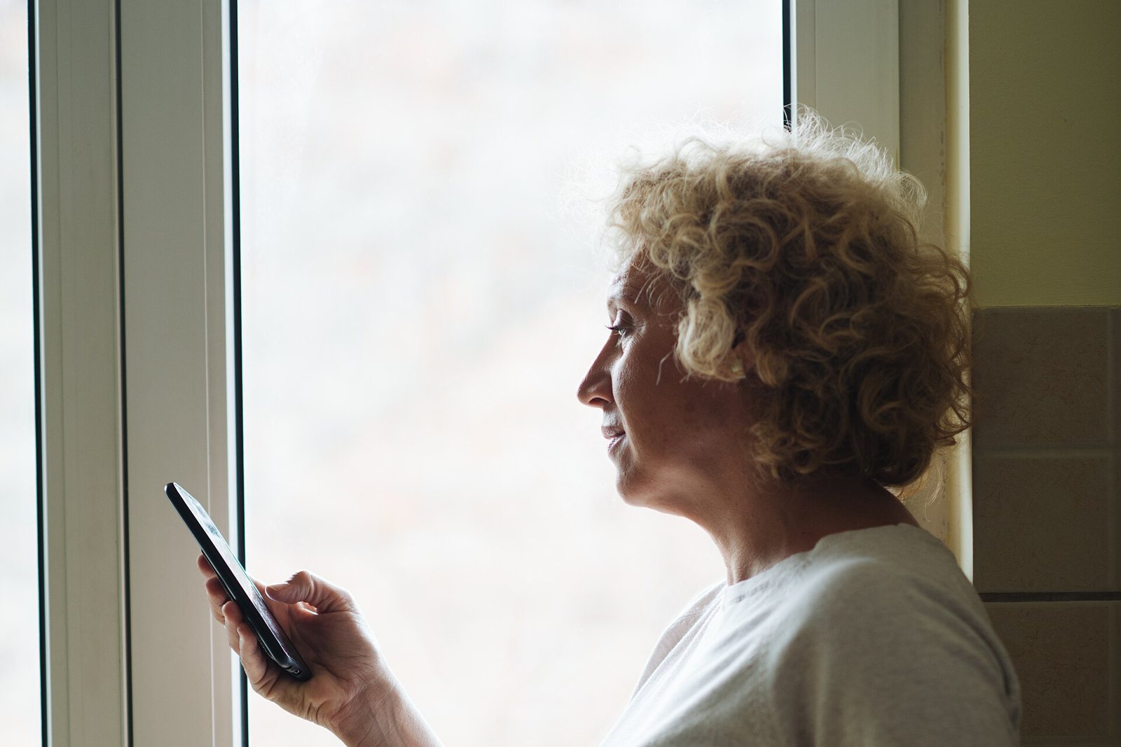 Older woman standing by a window checking her phone